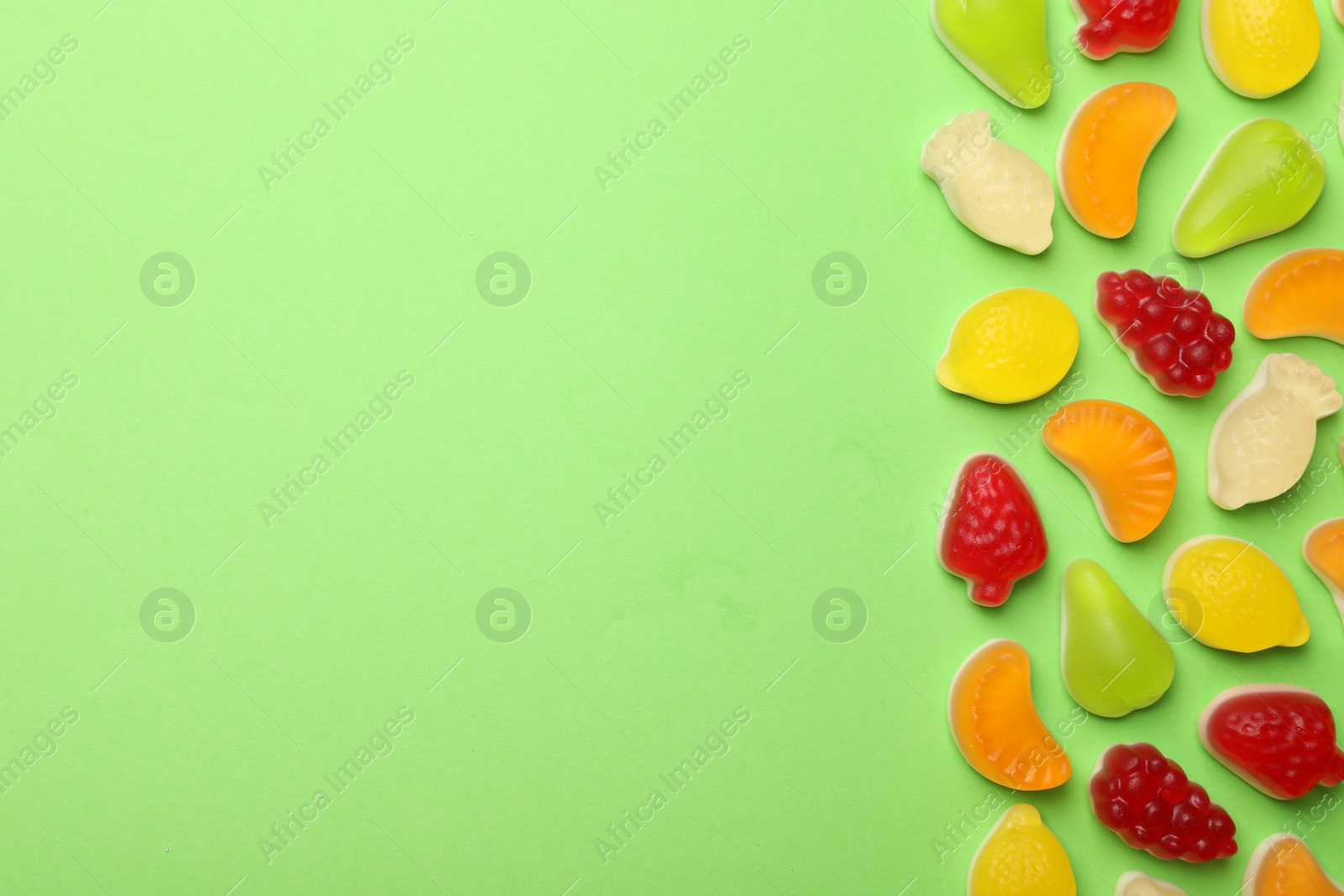 Photo of Delicious gummy fruit shaped candies on green background, flat lay. Space for text