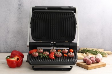 Photo of Electric grill with vegetables, meat balls and rosemary on wooden table