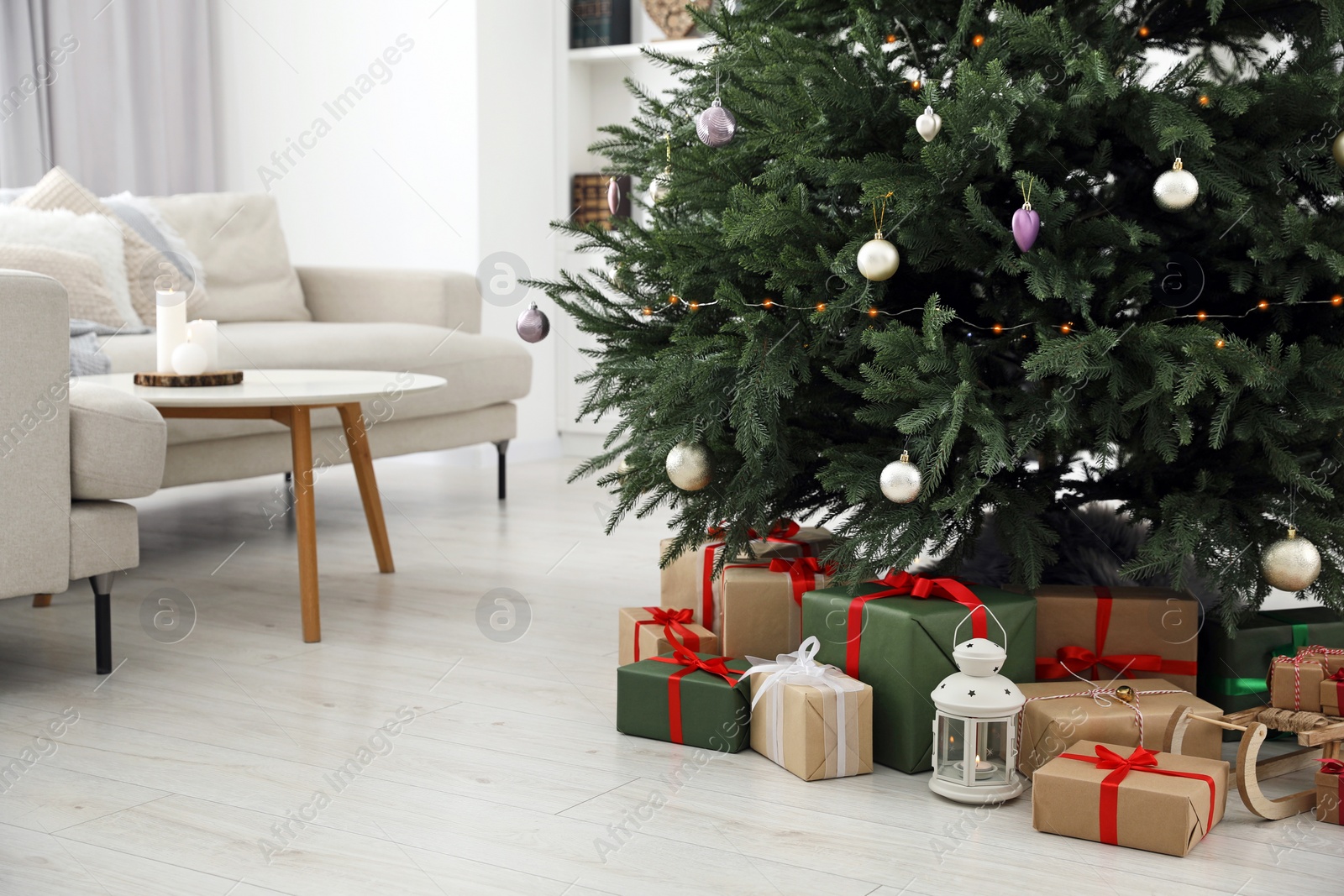 Photo of Beautifully wrapped gift boxes and lantern under Christmas tree in living room