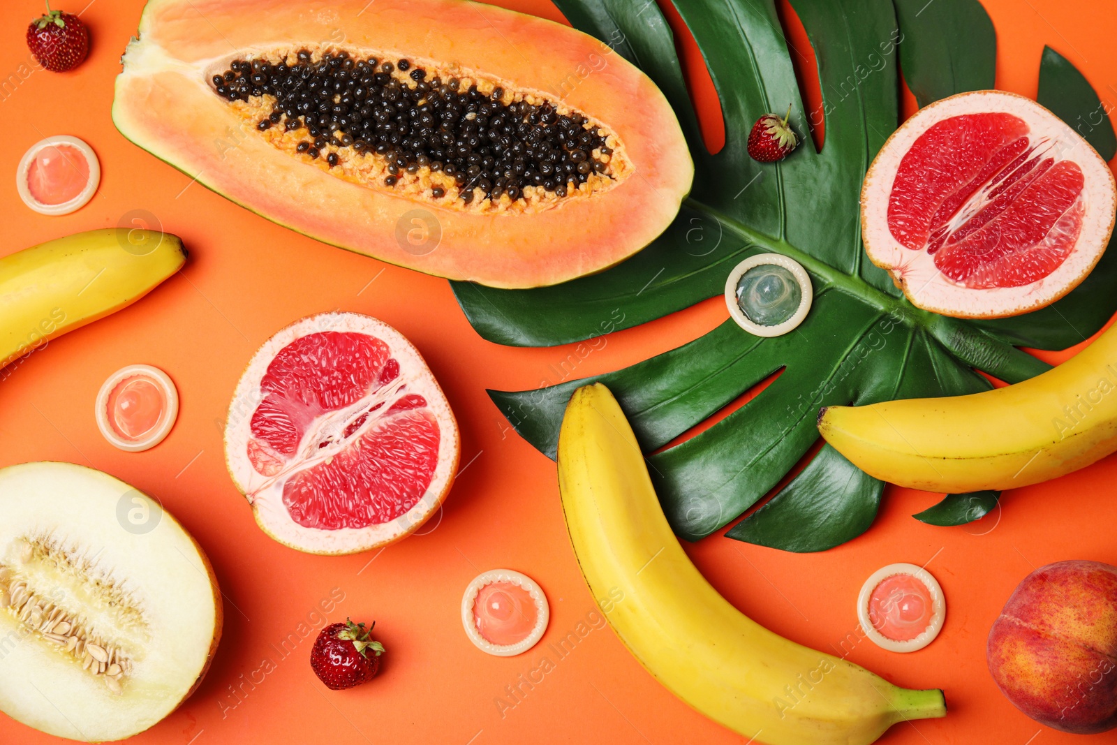 Photo of Flat lay composition with condoms and exotic fruits on orange background. Erotic concept