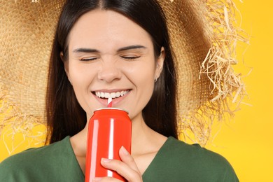 Beautiful happy woman drinking from red beverage can on yellow background, closeup