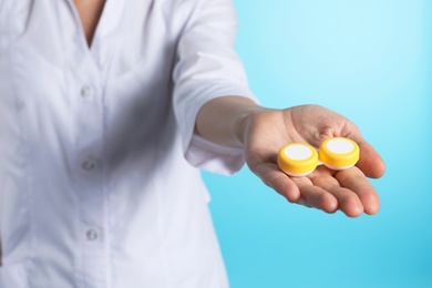 Photo of Female doctor holding contact lens case on color background, closeup. Medical object