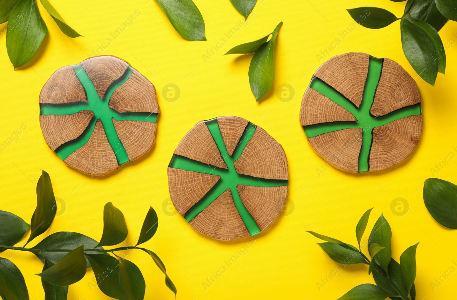 Photo of Stylish wooden cup coasters and green leaves on yellow background, flat lay