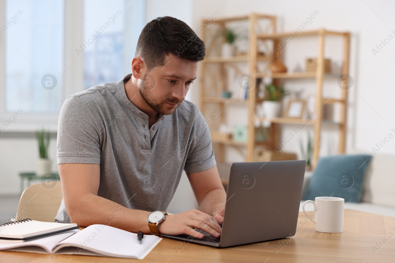 Photo of Man working on laptop at wooden desk in room