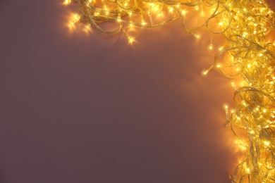 Photo of Glowing Christmas lights on violet background, top view. Space for text