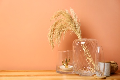 Vase with spikelets and decoration on wooden table near brown wall. Interior design