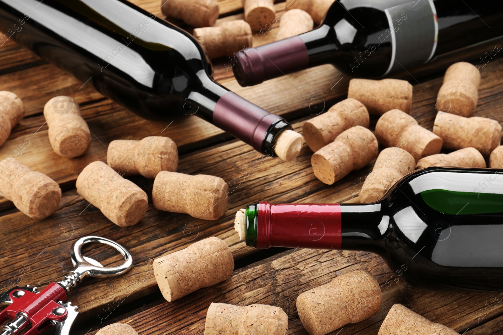 Photo of Bottles with wine, corkscrew and corks on wooden table