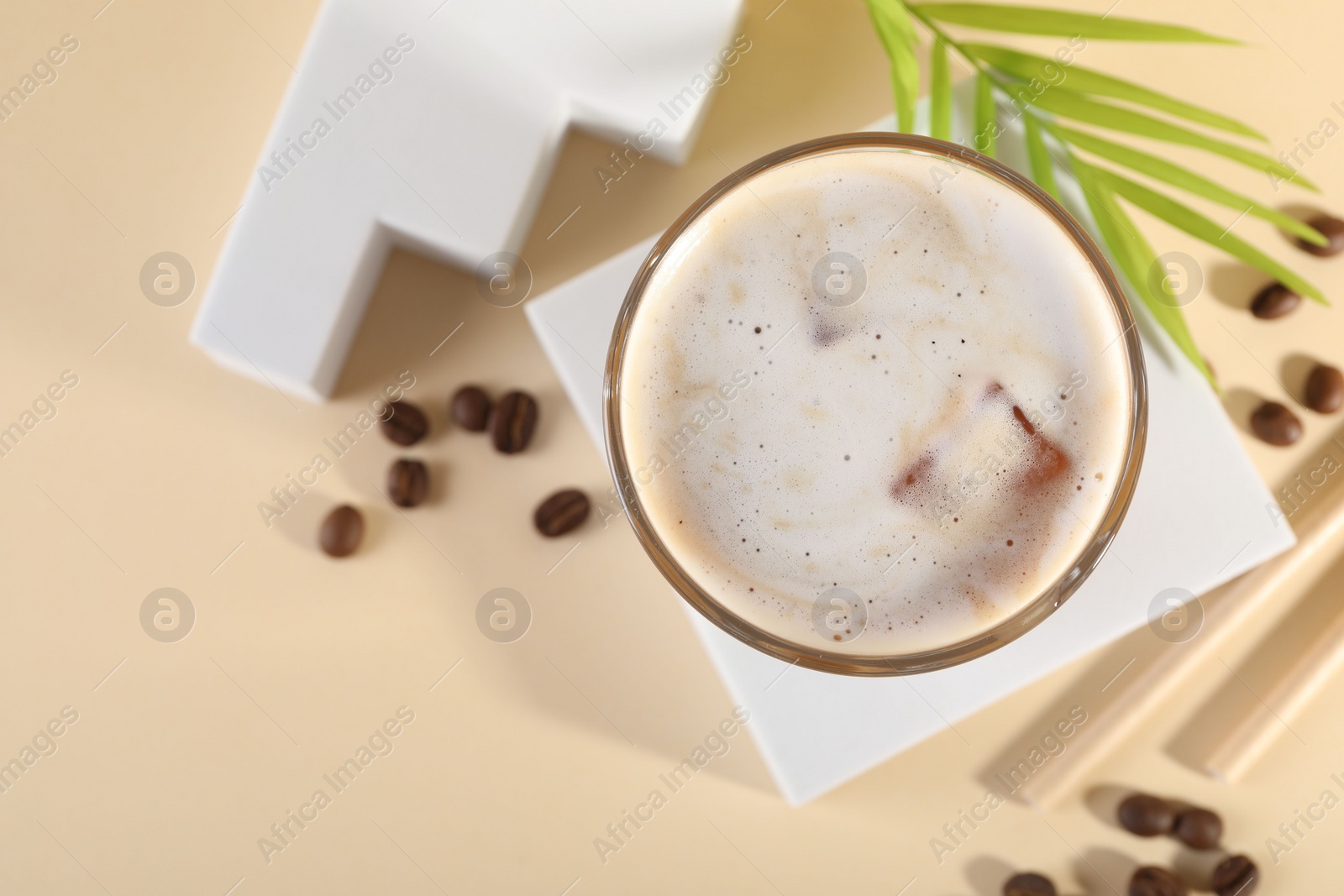 Photo of Refreshing iced coffee with milk in glass and beans on pale yellow table, top view. Space for text