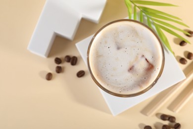 Photo of Refreshing iced coffee with milk in glass and beans on pale yellow table, top view. Space for text