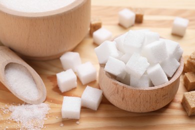 Photo of Bowls and scoop with different types of white sugar on wooden table, closeup