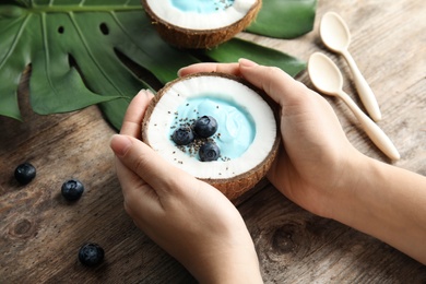 Photo of Woman holding coconut with spirulina smoothie on wooden table, closeup
