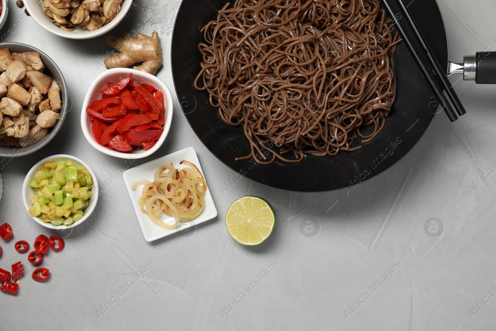 Photo of Wok with noodles, chicken and other products on light grey table, flat lay