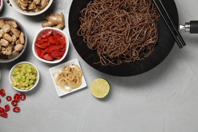 Wok with noodles, chicken and other products on light grey table, flat lay