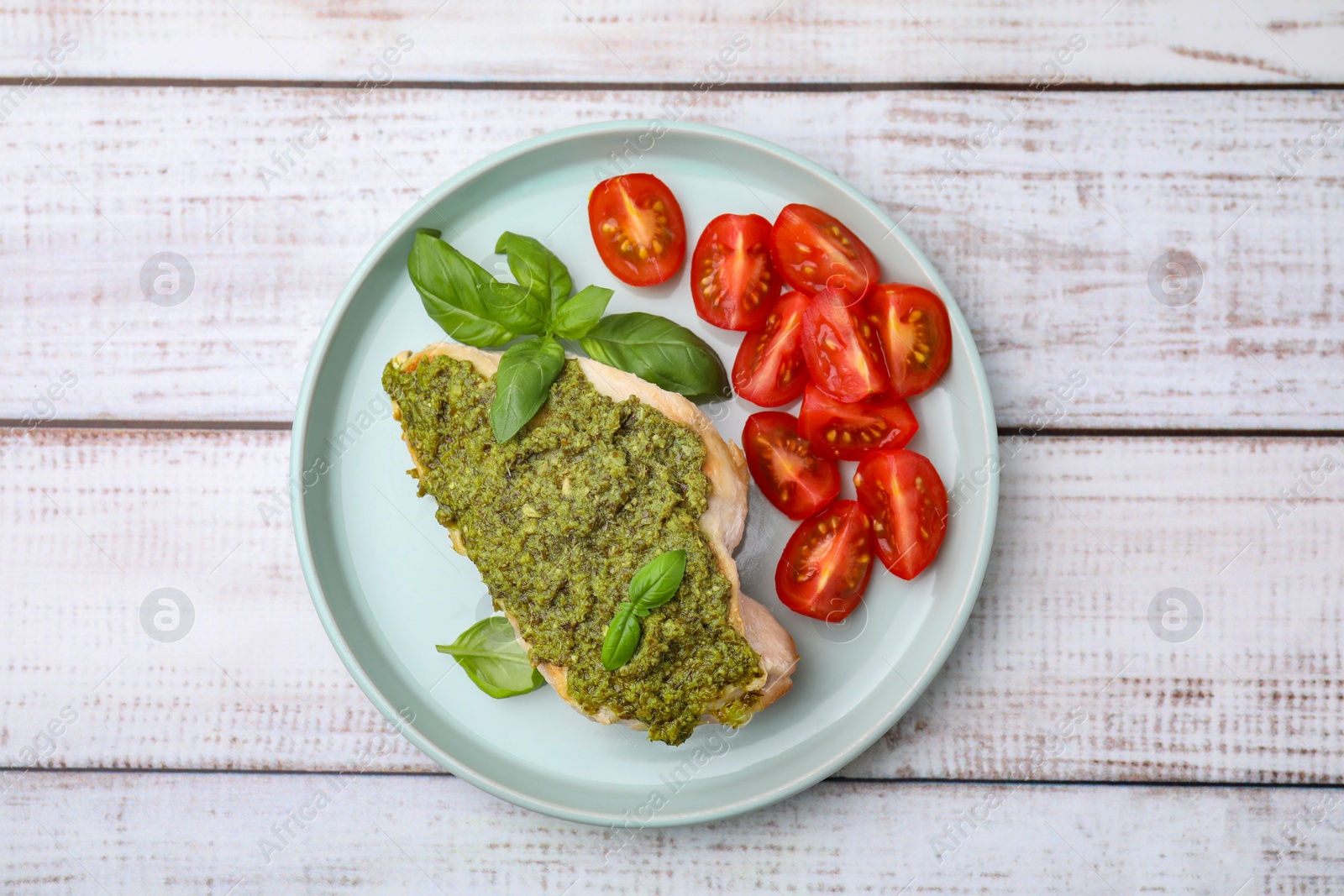 Photo of Delicious chicken breast with pesto sauce, tomatoes and basil on white wooden table, top view