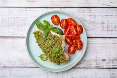 Photo of Delicious chicken breast with pesto sauce, tomatoes and basil on white wooden table, top view