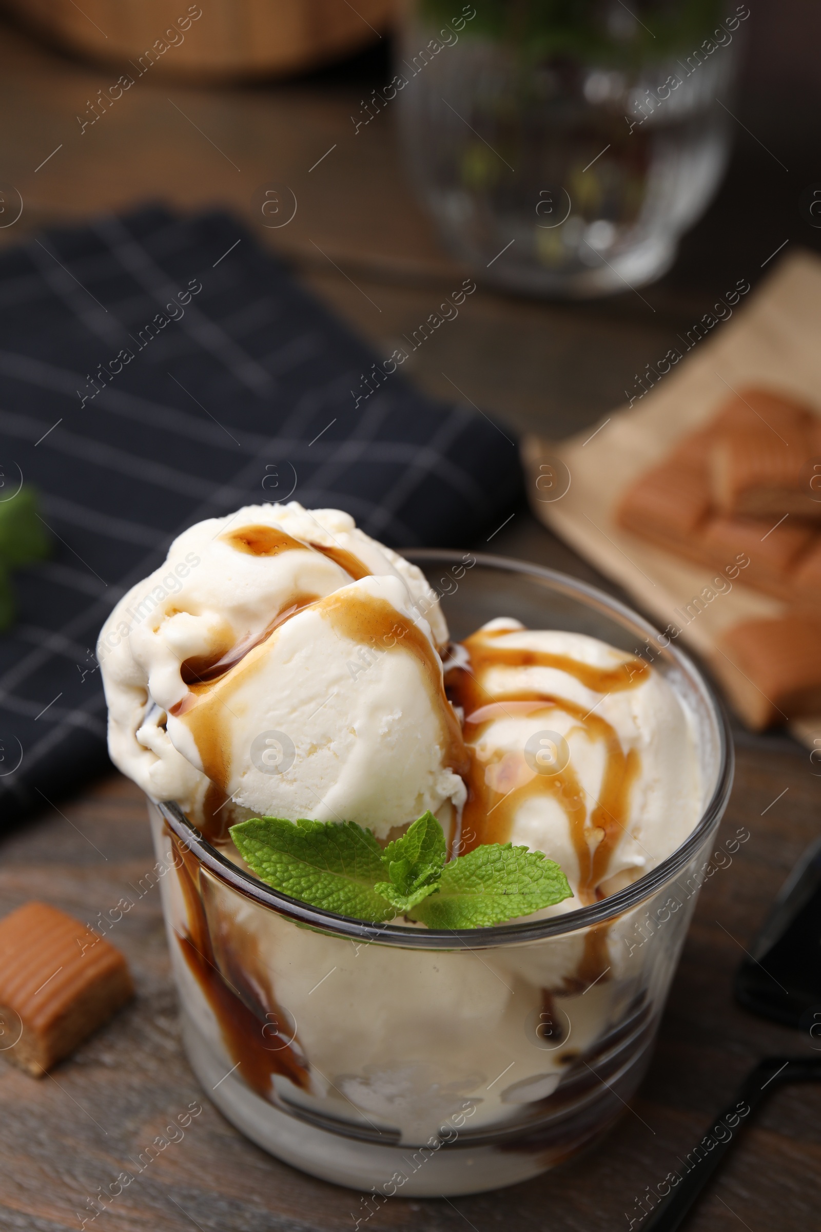 Photo of Scoops of ice cream with caramel sauce and mint leaves on wooden table, closeup