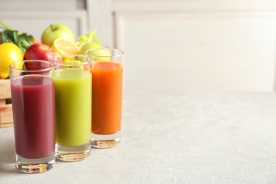 Photo of Three glasses of juices and wooden crate with fresh ingredients on light table. Space for text