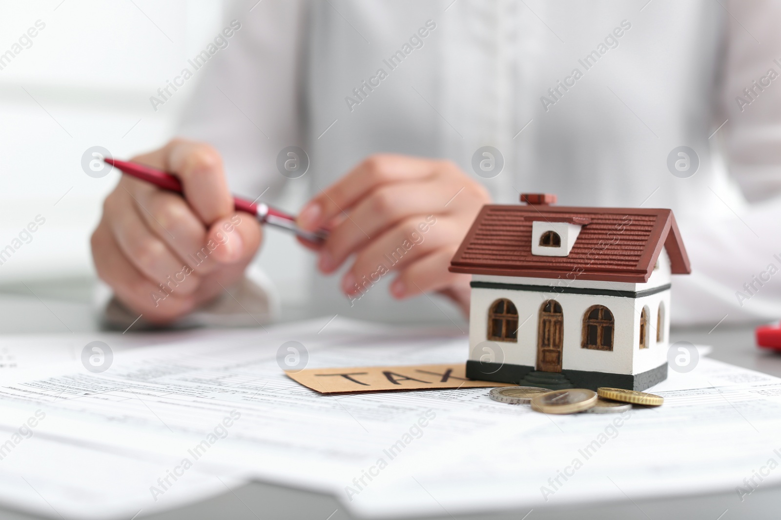 Photo of House model, coins and blurred woman on background. Tax day
