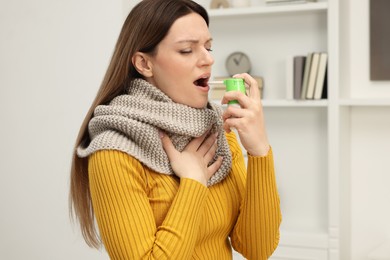 Adult woman with scarf using throat spray at home