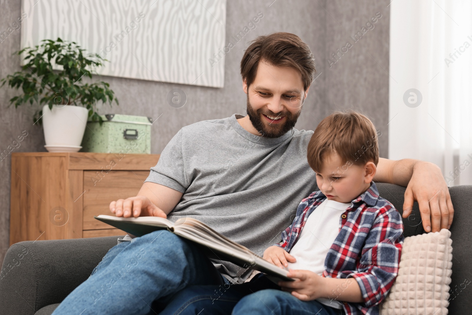 Photo of Dad and son reading book together on sofa at home