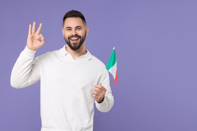 Photo of Young man with flag of Italy showing ok gesture on purple background, space for text