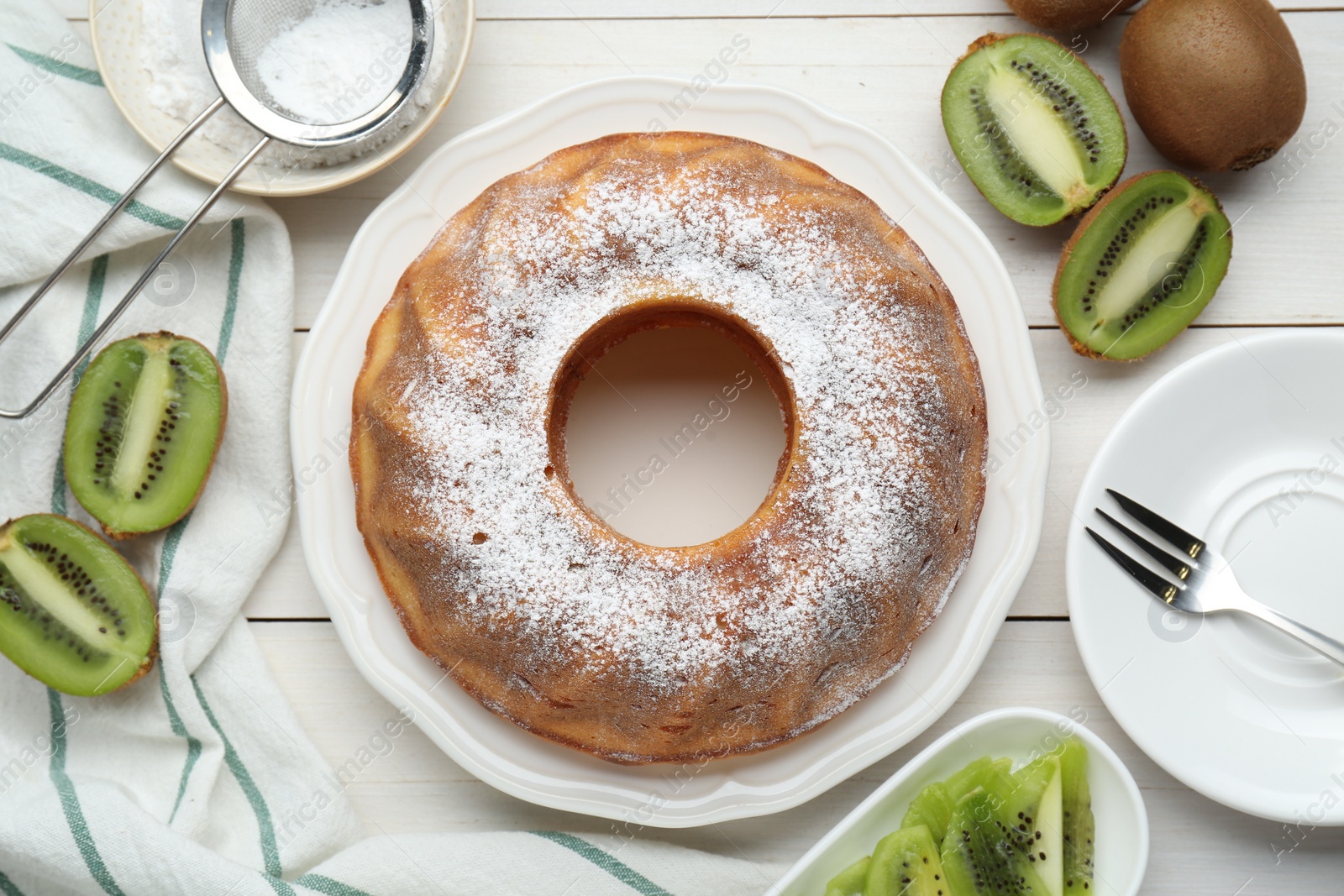 Photo of Homemade yogurt cake with kiwi and powdered sugar on white wooden table, flat lay