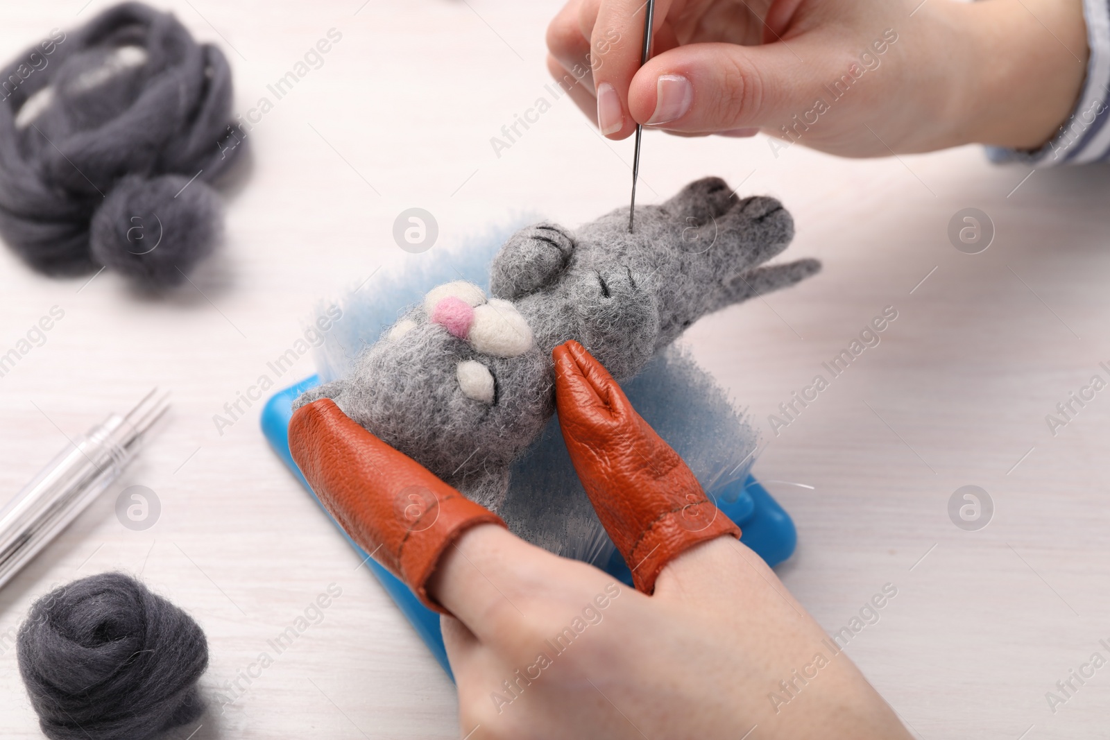 Photo of Woman felting toy cat from wool at light wooden table, closeup