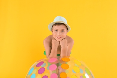 Cute little child in beachwear with bright inflatable ball on yellow background