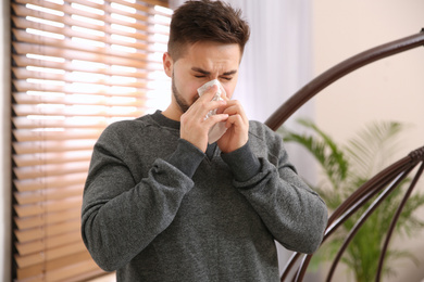 Photo of Sick young man sneezing at home. Influenza virus