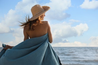 Woman with beach towel and straw hat near sea, back view, space for text