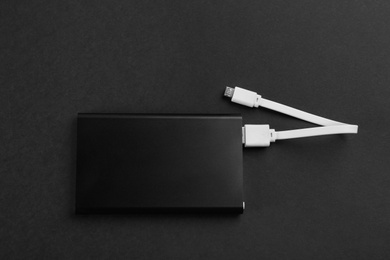 Photo of Modern portable charger with cable on black background, top view