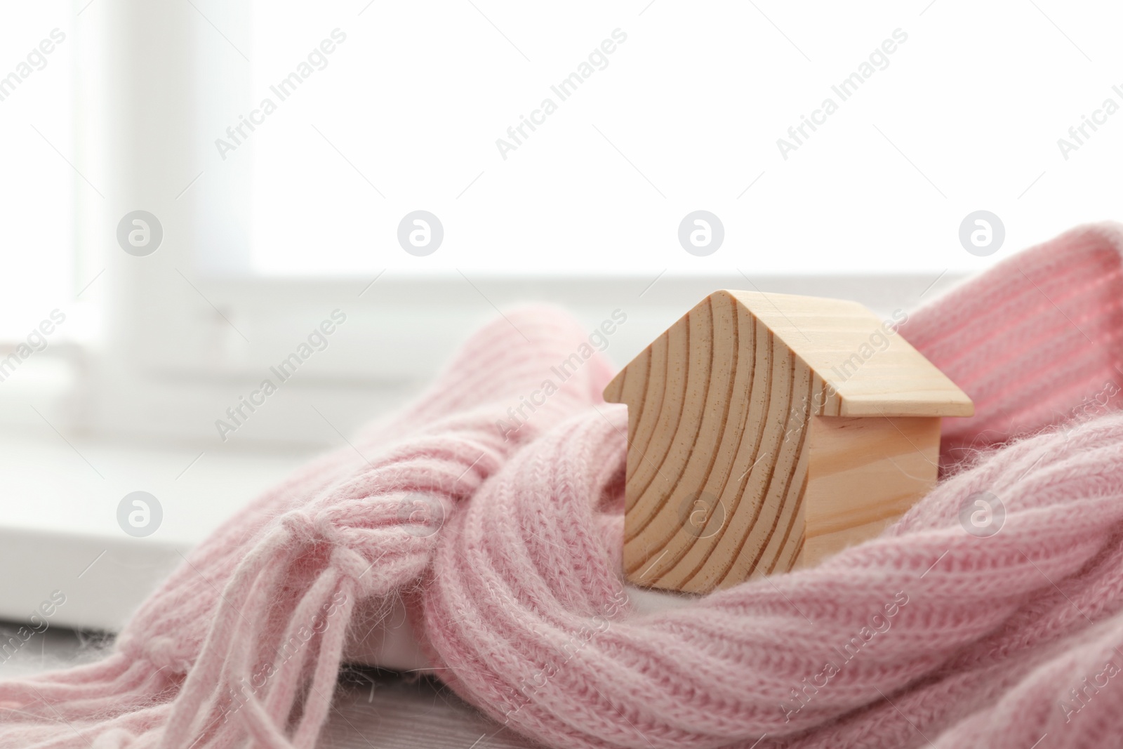 Photo of Wooden house model wrapped in pink scarf on windowsill indoors, space for text. Heating efficiency