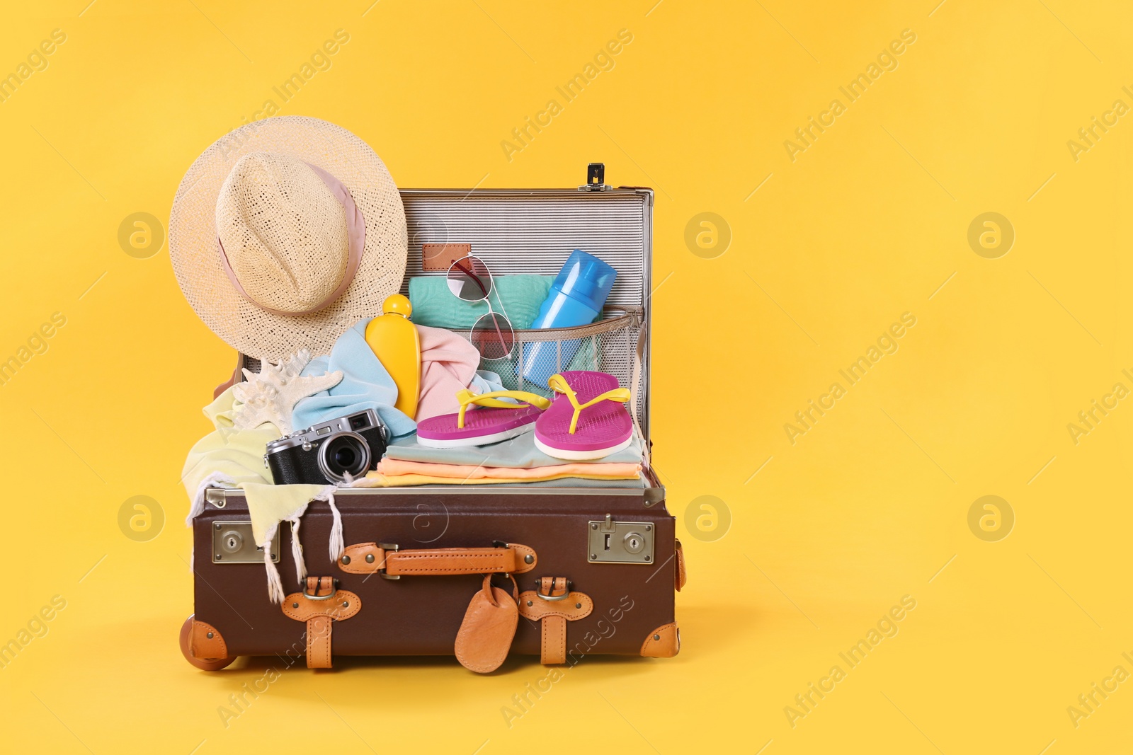 Photo of Packed vintage suitcase with different beach objects on orange background, space for text. Summer vacation