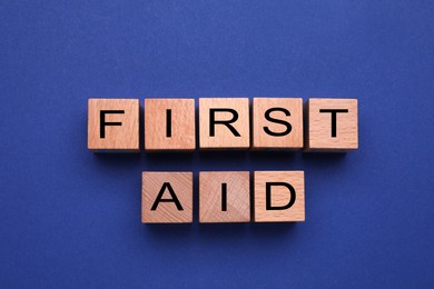 Photo of Words First Aid made of wooden cubes on blue background, flat lay