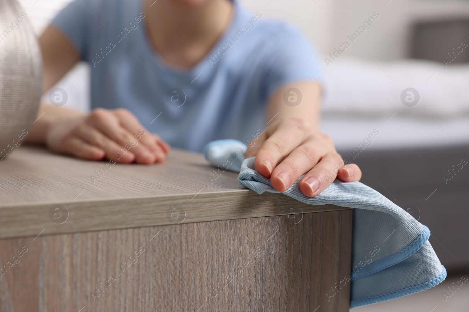 Photo of Woman with microfiber cloth cleaning wooden chest of drawers in room, closeup