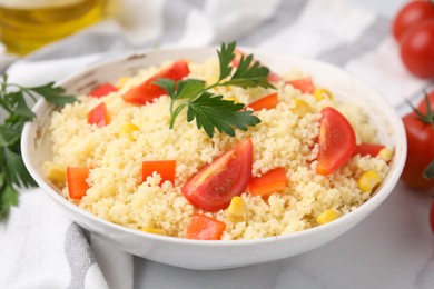 Photo of Tasty couscous with parsley, corn and tomatoes in bowl on white table, closeup