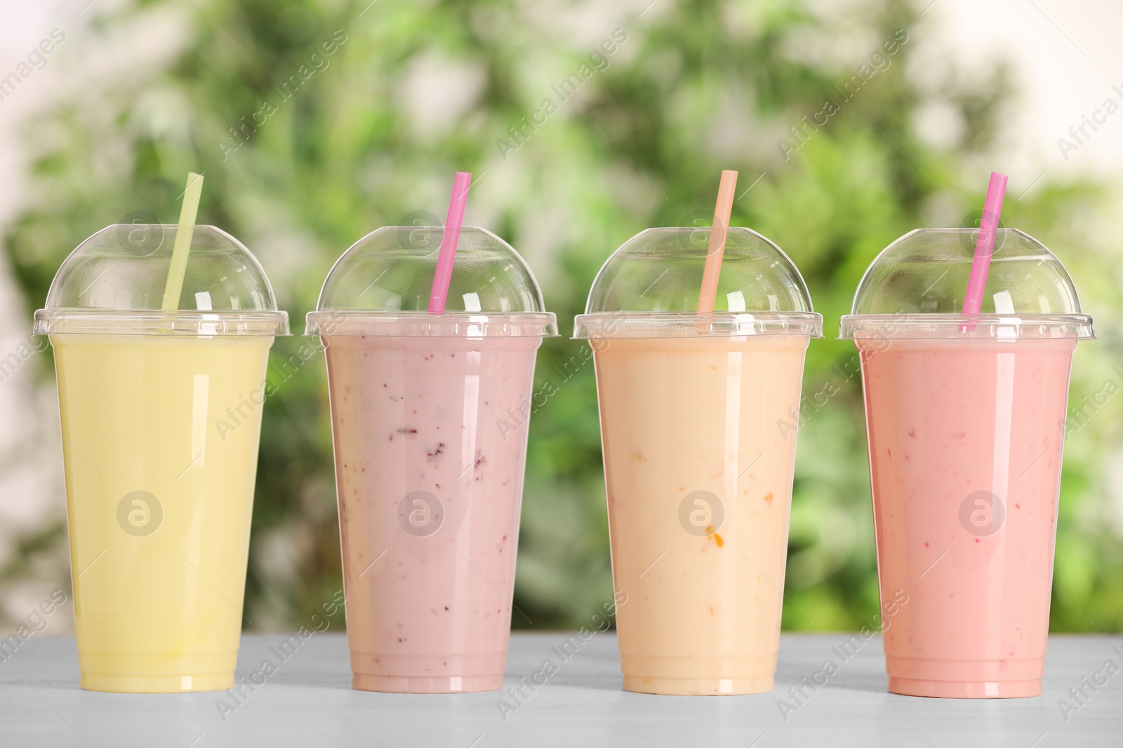 Photo of Plastic cups with different tasty smoothies on wooden table outdoors