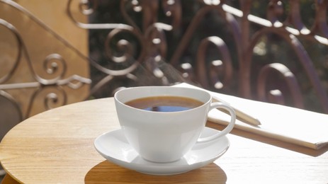 Cup of aromatic coffee, pen and newspaper on wooden table outdoors