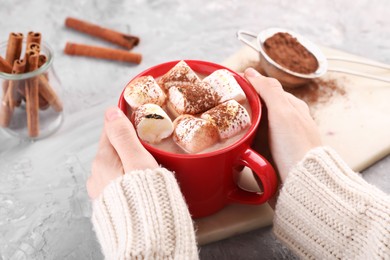 Photo of Woman drinking aromatic hot chocolate with marshmallows and cocoa powder at gray table, closeup