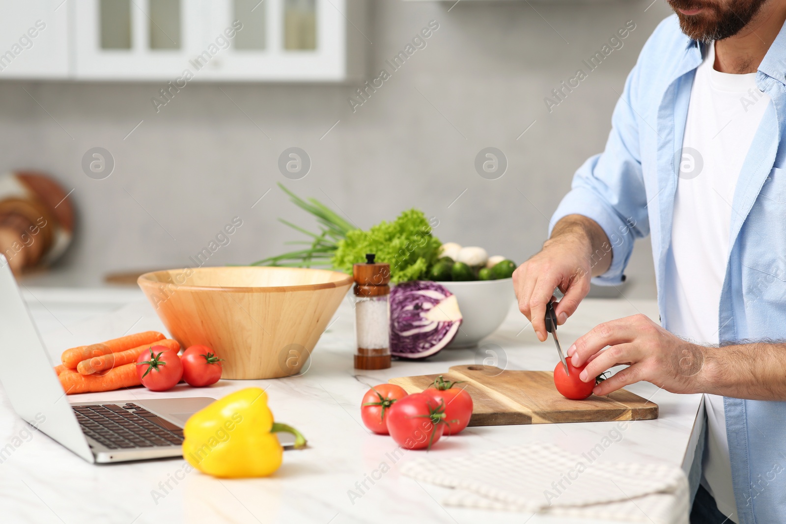 Photo of Man making dinner while watching online cooking course via laptop in kitchen, closeup