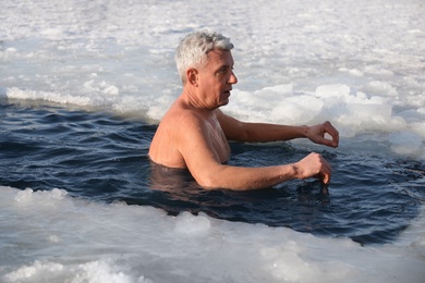 Photo of MYKOLAIV, UKRAINE - JANUARY 06, 2021: Mature man immersing in icy water on winter day