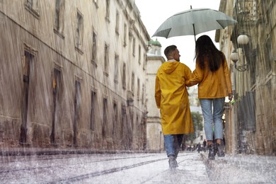 Image of Lovely young couple with umbrella walking under rain on city street, back view
