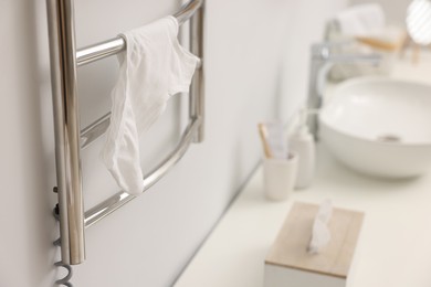 Photo of Heated towel rail with underwear on white wall in bathroom, closeup