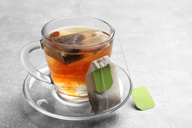 Photo of Tea bags and glass cup of hot beverage on light table, closeup. Space for text