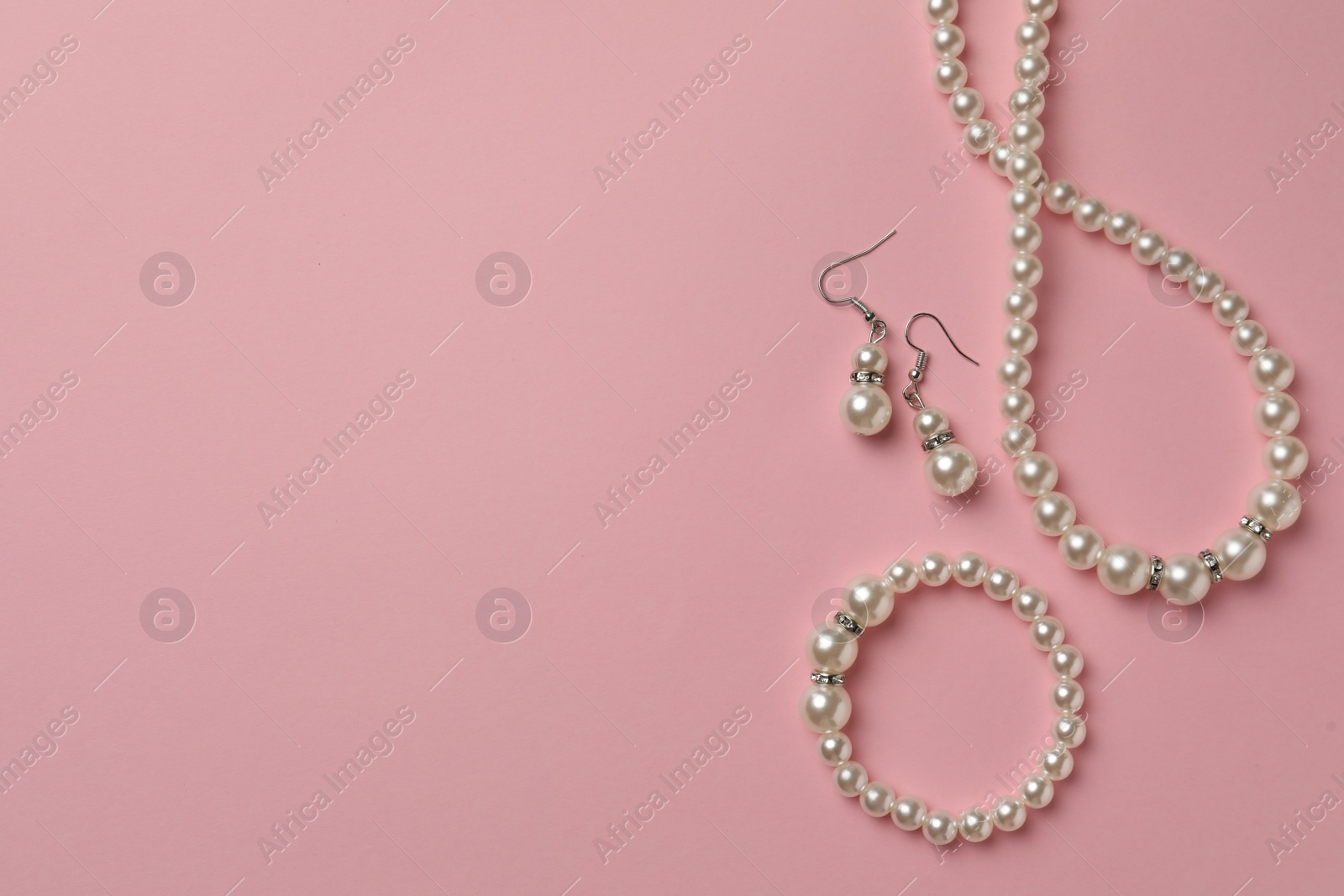 Photo of Elegant necklace, bracelet and earrings with pearls on pink background, flat lay. Space for text