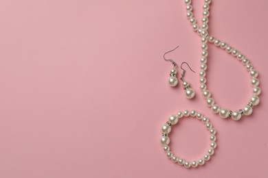 Photo of Elegant necklace, bracelet and earrings with pearls on pink background, flat lay. Space for text