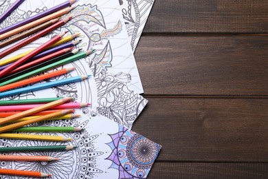 Photo of Antistress coloring pages and pencils on wooden table, flat lay. Space for text