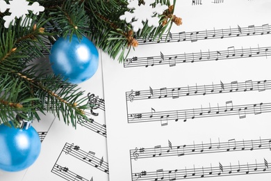 Fir branches, decorative snowflakes and light blue balls on Christmas music sheets, flat lay