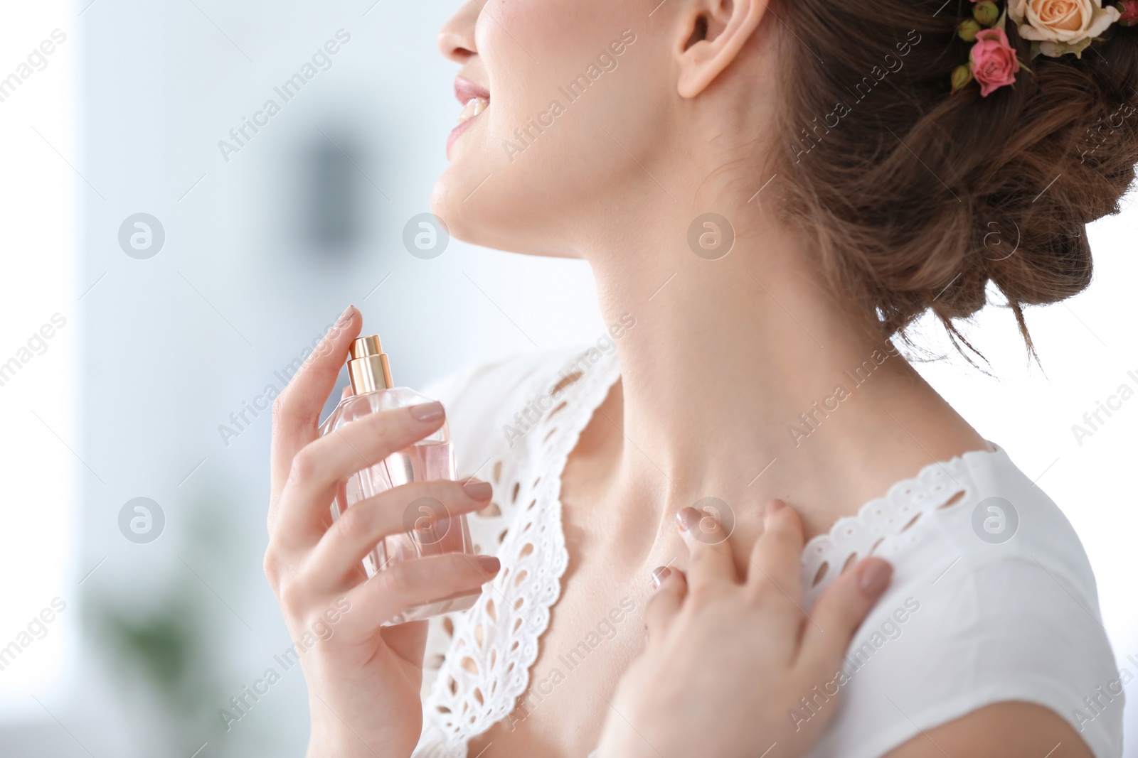 Photo of Beautiful young woman with bottle of perfume on blurred background, closeup
