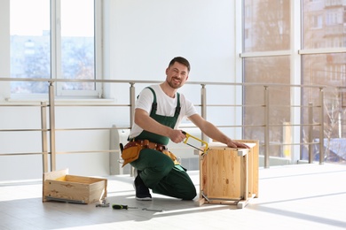 Photo of Carpenter in uniform making furniture indoors. Professional construction tools